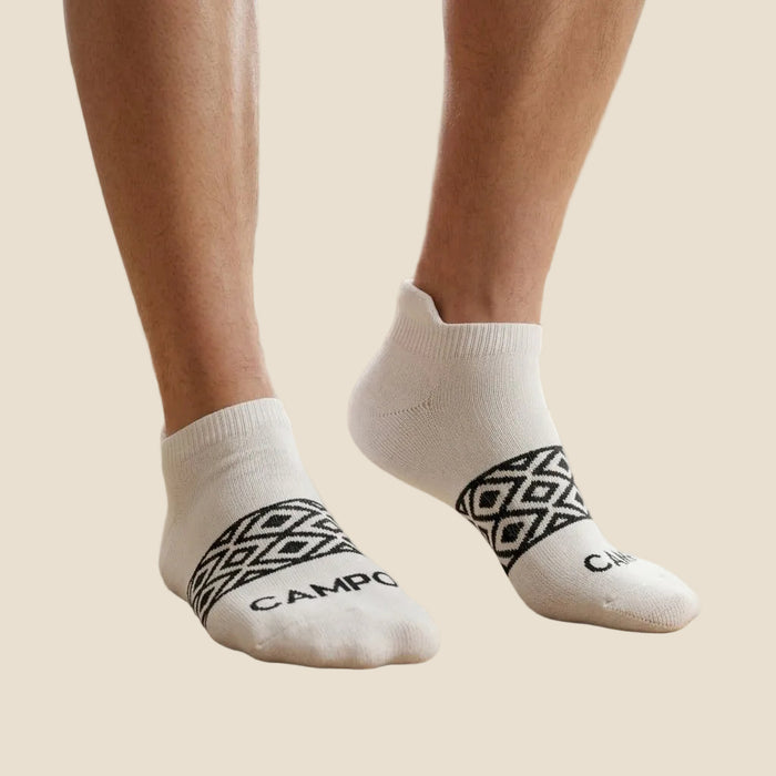 White socks with black patterns and 'CAMP' branding worn by a person on a wooden floor.