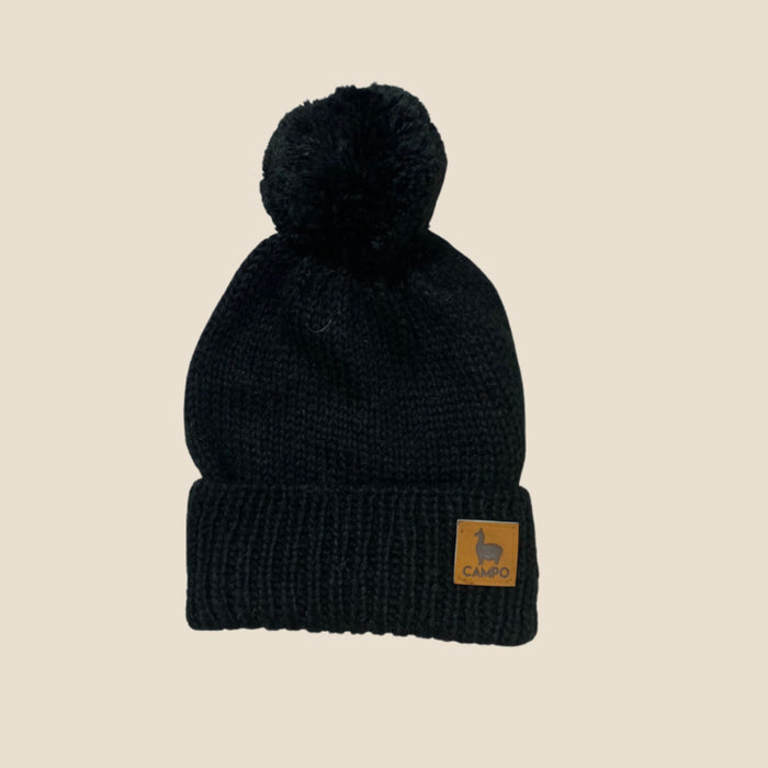 Black knit beanie with pom-pom on a beige background