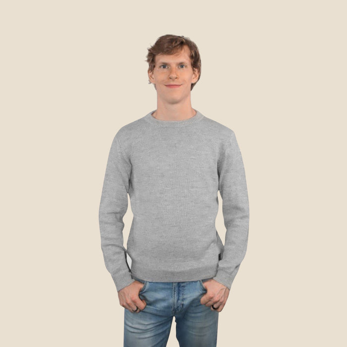 Man wearing a light gray sweater and blue jeans against a beige background