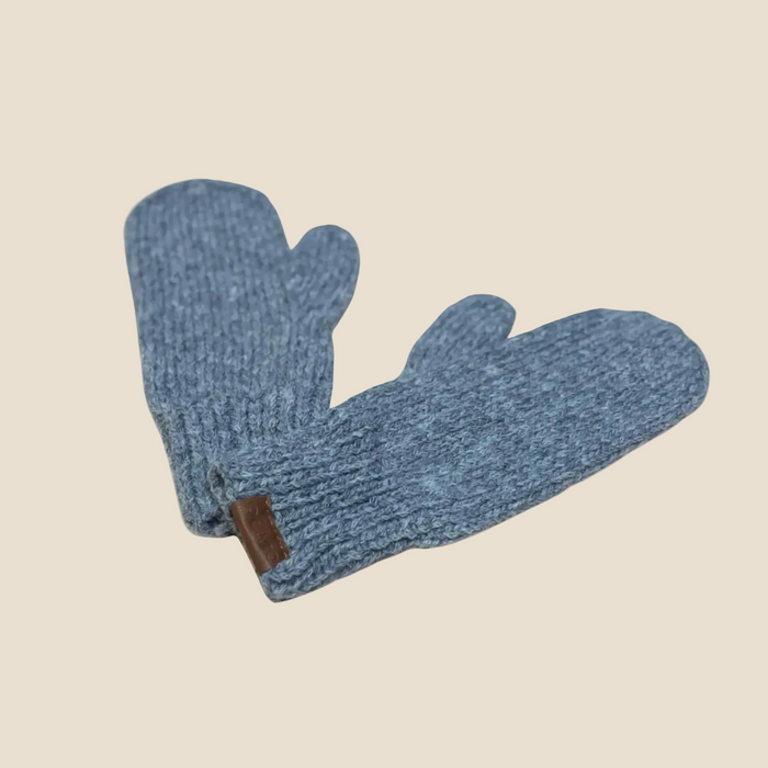 A pair of heathered blue knit mittens with a small brown leather tab, displayed on a solid pale beige background.