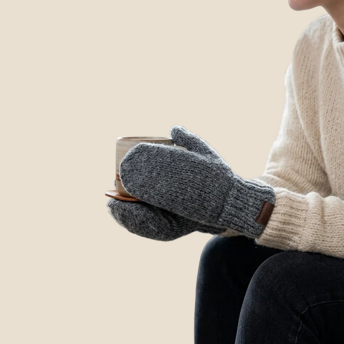 Person wearing gray gloves holding a mug in a cozy indoor setting