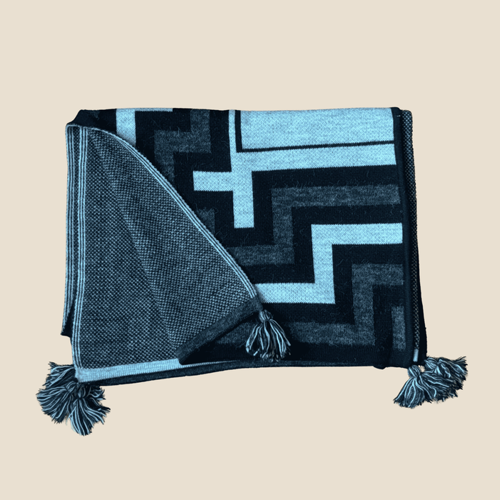 Black and gray patterned throw blanket with tassels on a beige background