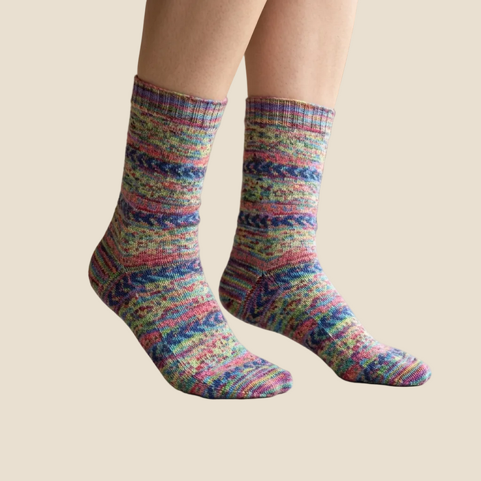 Multicolored patterned socks worn by a person on a light wooden floor.