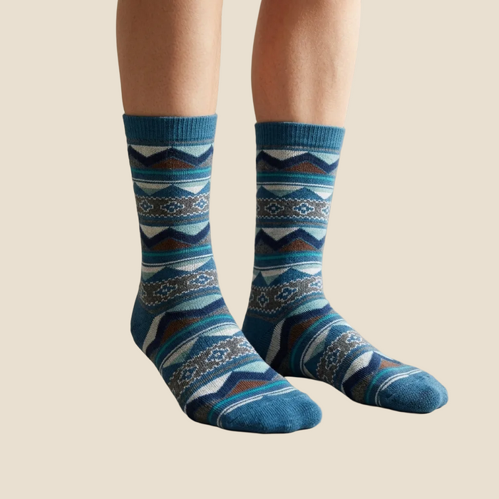 Blue patterned socks worn by a person sitting on a chair with books in the background.