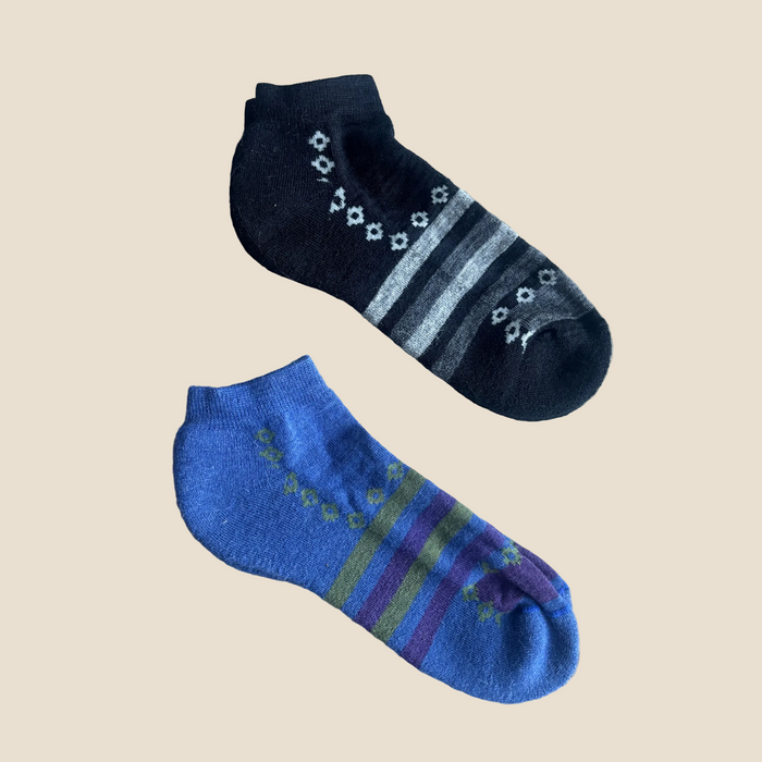 Two pairs of socks, one black with white patterns and the other blue with green and purple stripes, on a wooden surface.