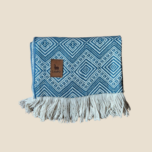 Blue patterned blanket with fringes and a brand logo on a beige background