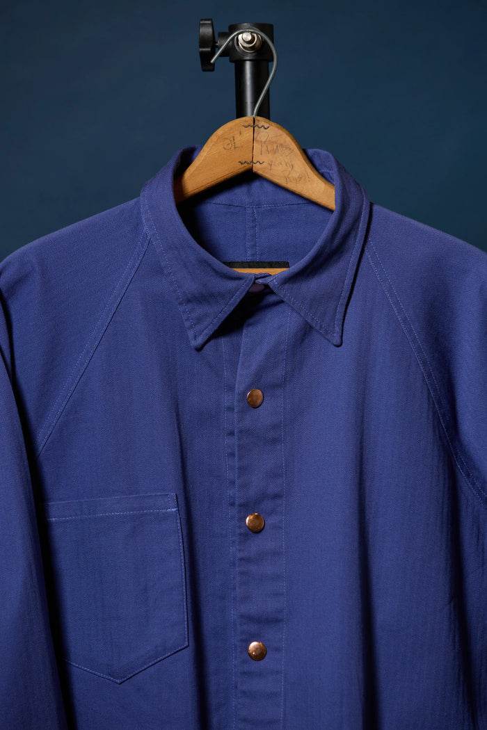 Barista Chore Coat in Washed Herringbonet on a wooden hanger against a dark background