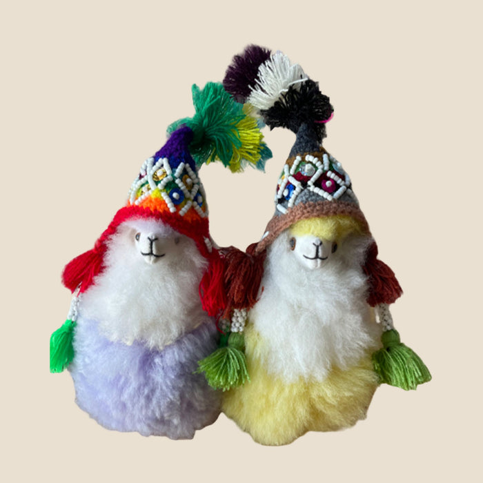 Two plush llamas wearing colorful hats on a beige background