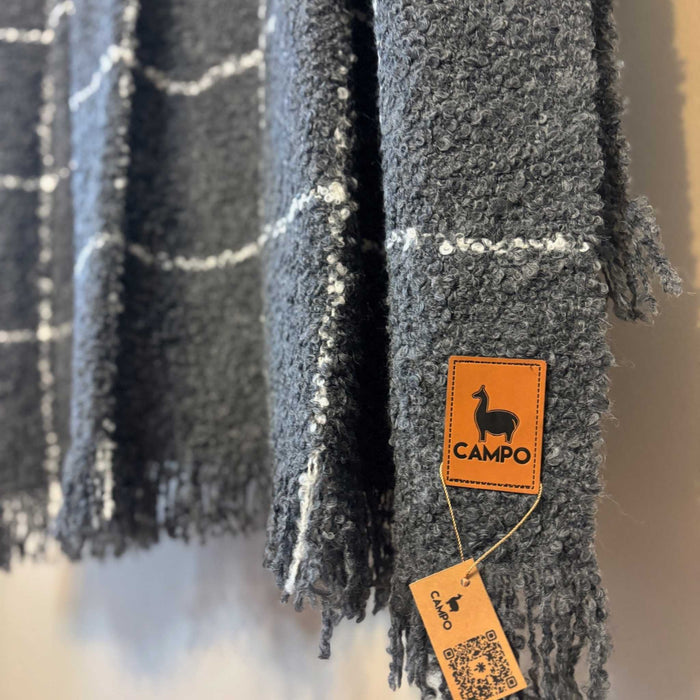 Gray plaid blanket with a 'Campo' brand tag on a blurred background