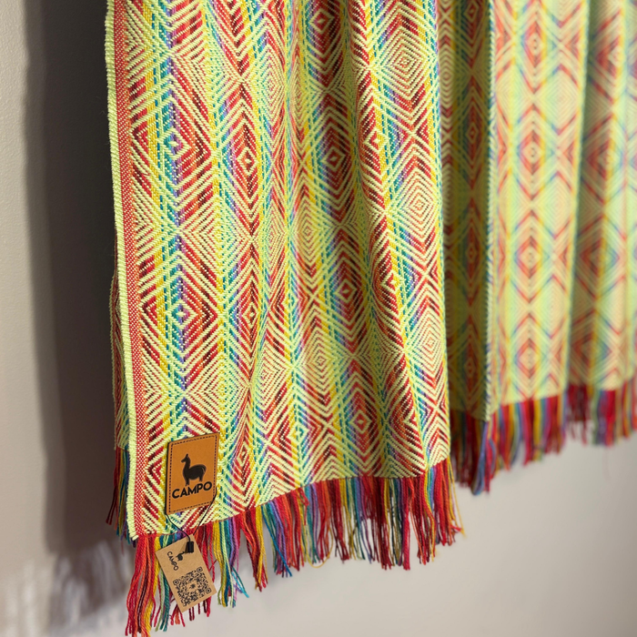 Colorful patterned fabric with fringes and a visible brand label on a plain background