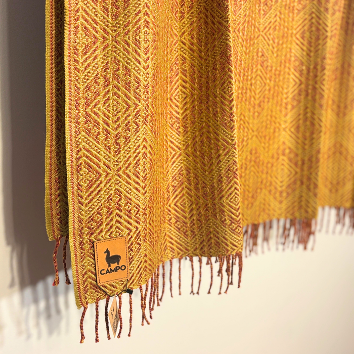 Yellow knitted blanket with a brand logo on a neutral background