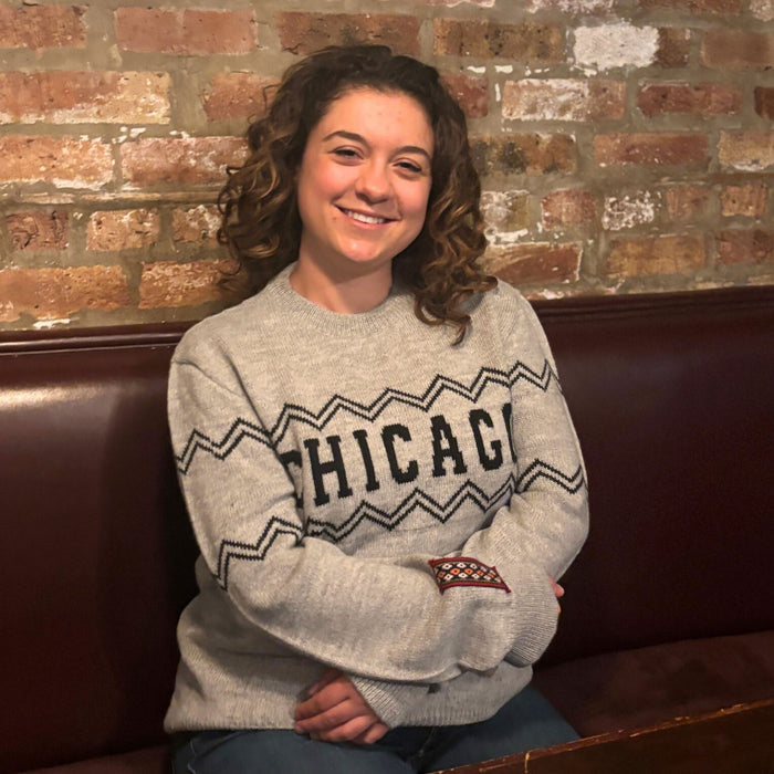 Person wearing a 'Chicago' sweater sitting on a couch against a brick wall.