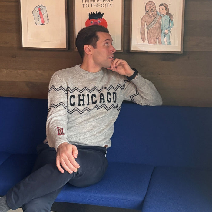 Man wearing a 'Chicago' sweater sitting on a blue couch with framed pictures on the wall.