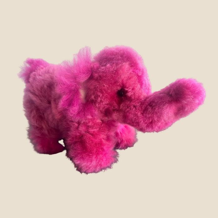 Pink plush elephant toy on a dark surface with a light gray background