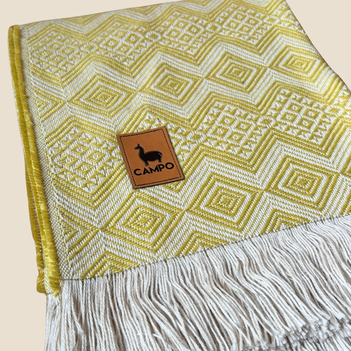 Yellow patterned blanket with a 'Campo' brand patch on a beige background