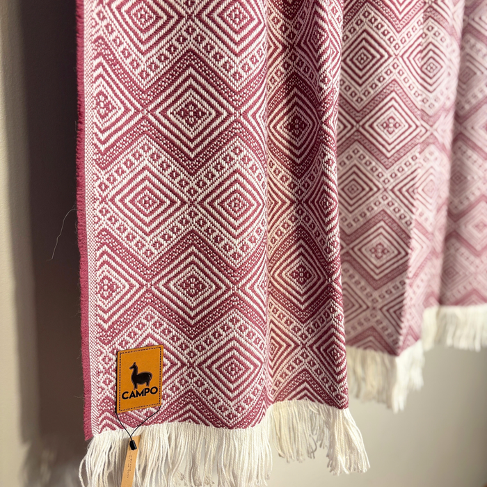 Red and white patterned fabric with tassels and a visible brand tag on a neutral background