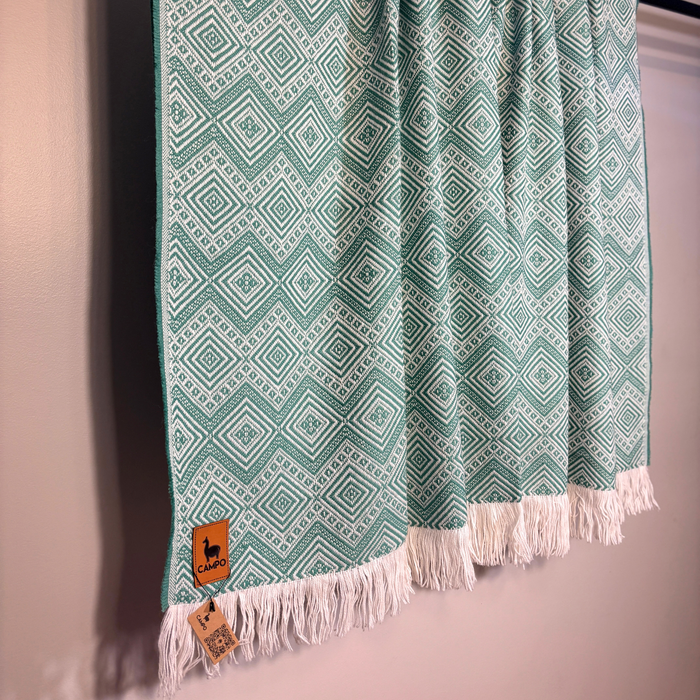 Green patterned throw blanket with white fringe on a pink background