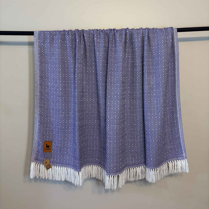 Purple patterned towel with white fringe draped over a black rod against a beige wall.