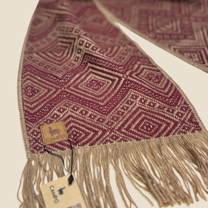 Patterned scarf with fringes and a brand tag on a beige background
