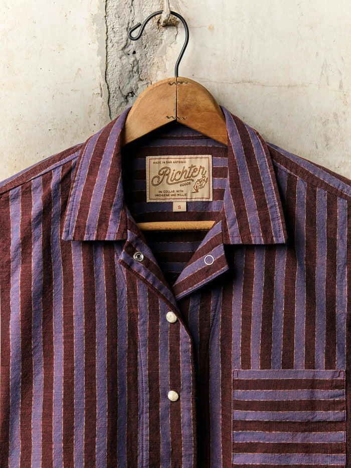 Striped shirt on a hanger with a visible brand label against a textured wall.