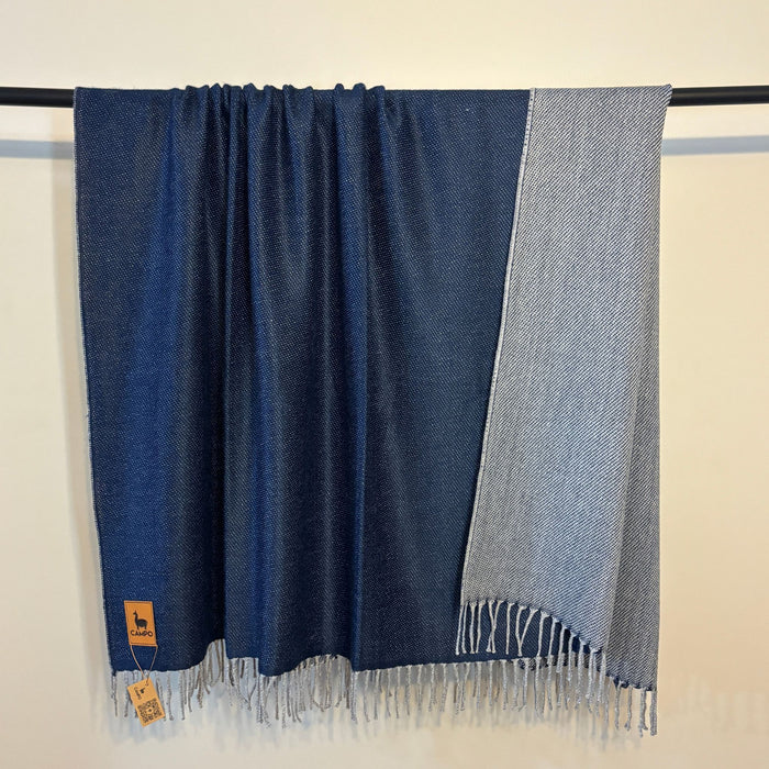 Blue and gray scarf with fringes on a black rod against a beige background