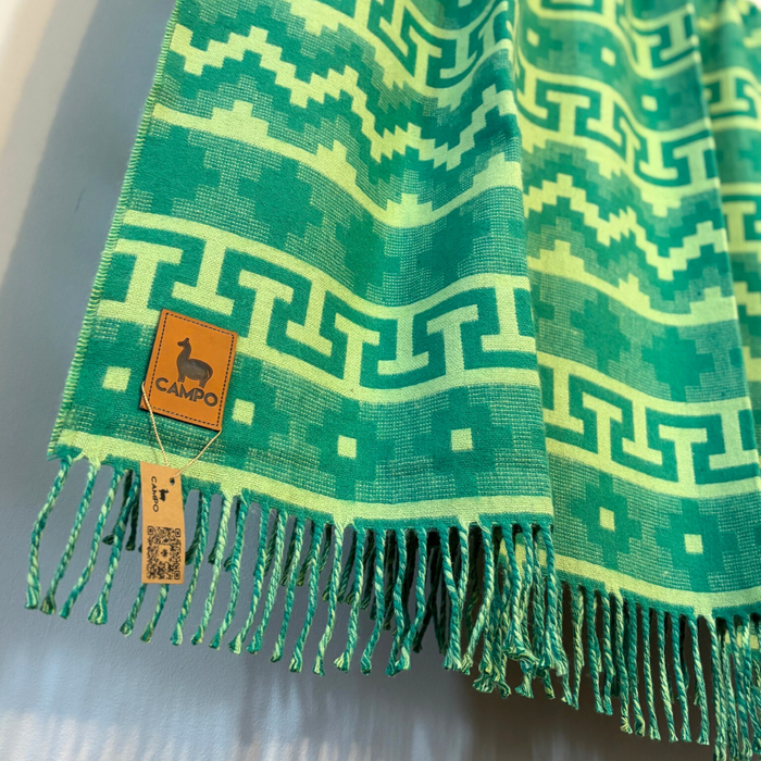 Green patterned fabric with fringes and a visible brand label on a gray background