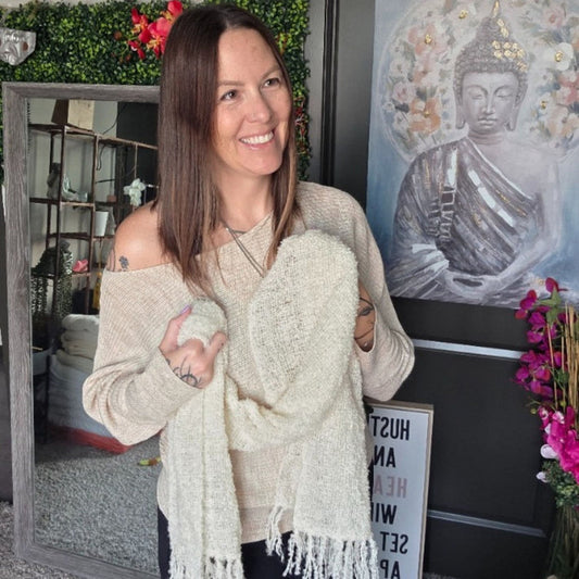 Woman holding a white scarf in a room with decor elements like a Buddha painting and plants.