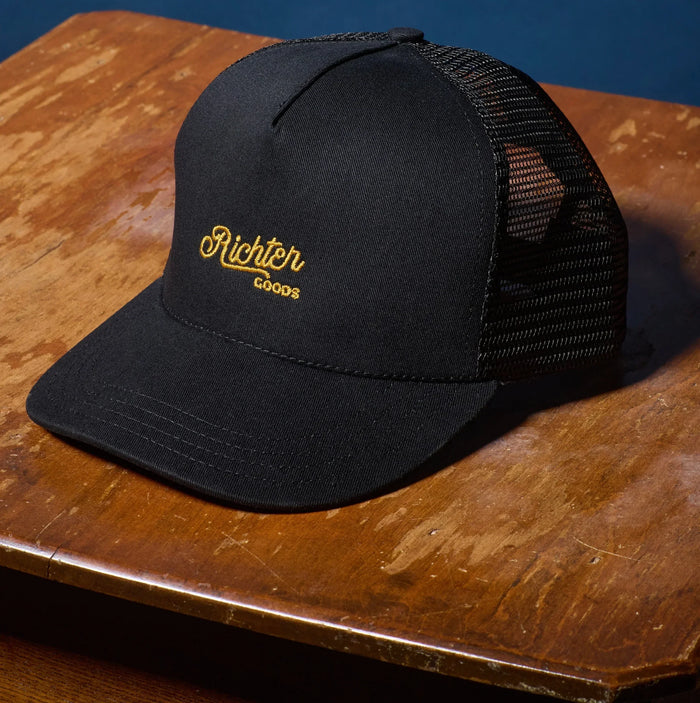 Richter Goods black mesh trucker hat front on wooden table