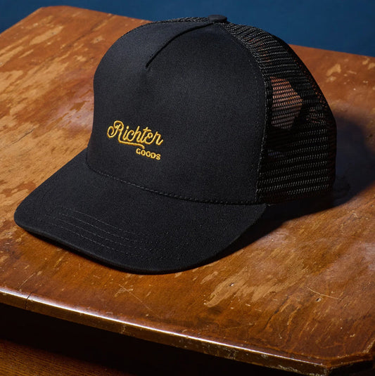 Richter Goods black mesh trucker hat front on wooden table