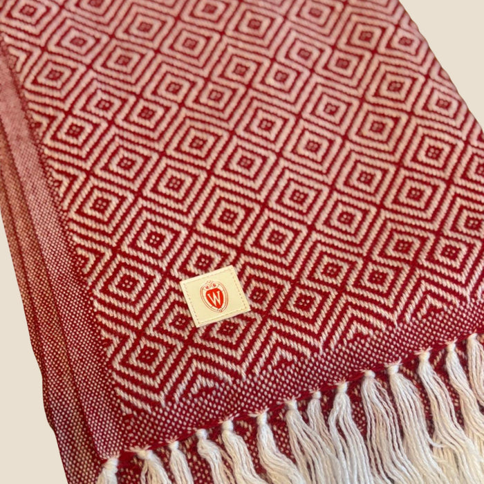 Red patterned fabric with white tassels and a small logo on a beige background