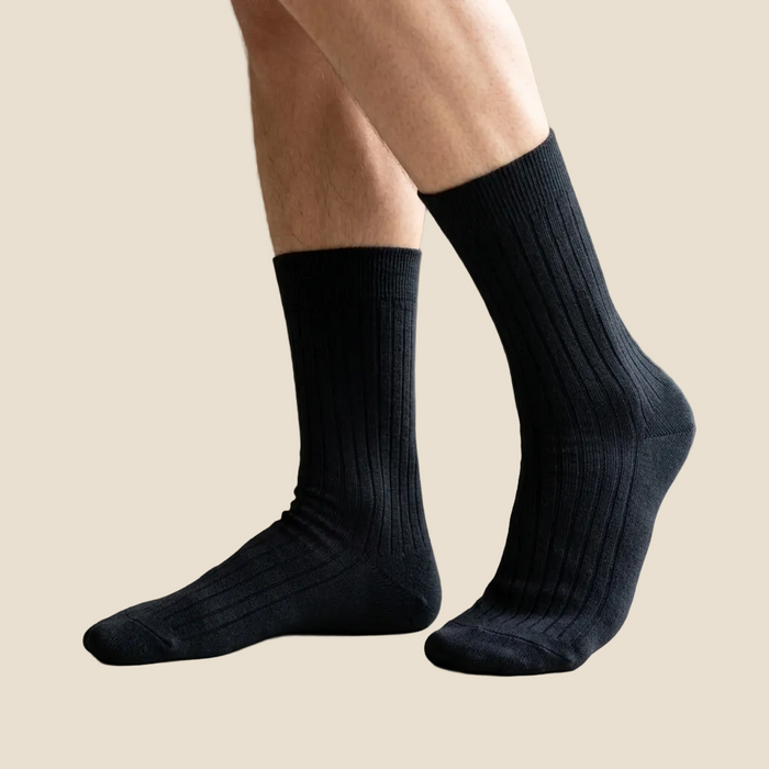 Person wearing black socks indoors with a neutral background