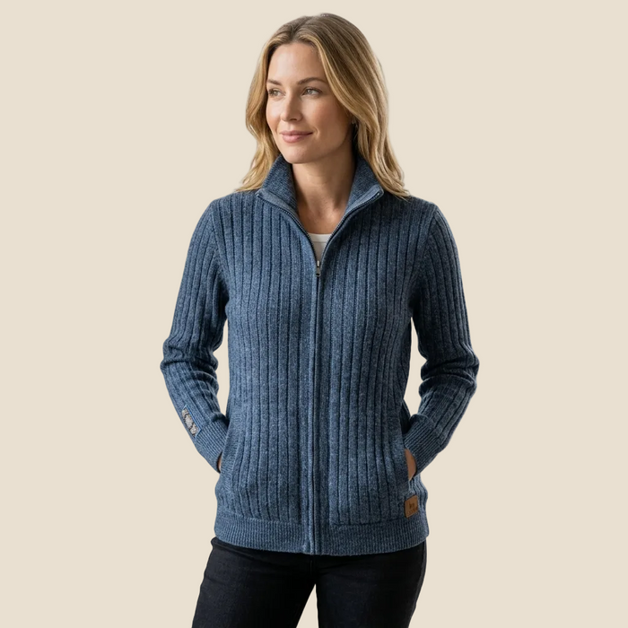 A woman wearing a blue ribbed zip-up sweater with a stand collar, shown against a plain beige background.