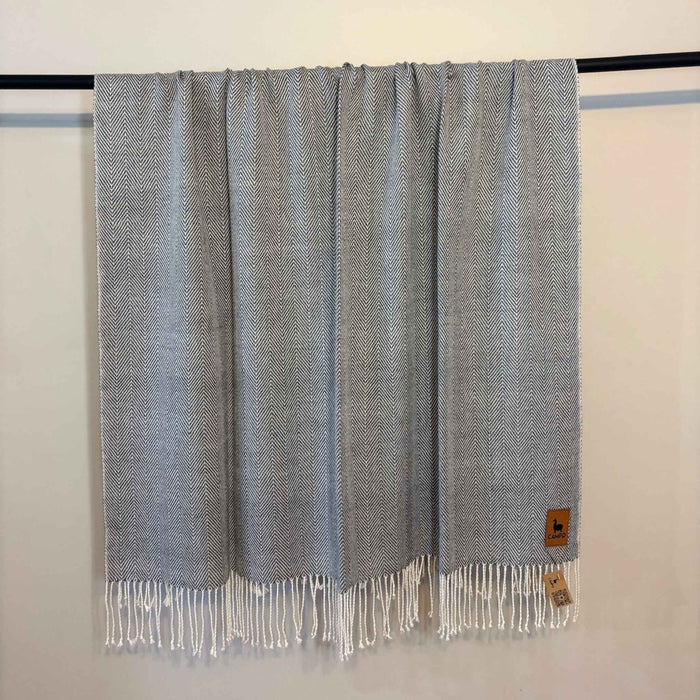 Gray woven blanket with fringes on a black rod against a white wall