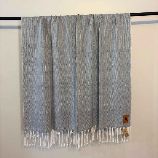 Gray woven blanket with fringes on a black rod against a white wall