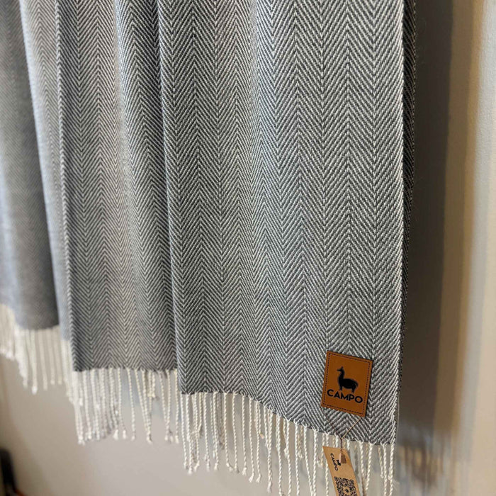 Gray herringbone patterned scarf with a brand tag on a neutral background