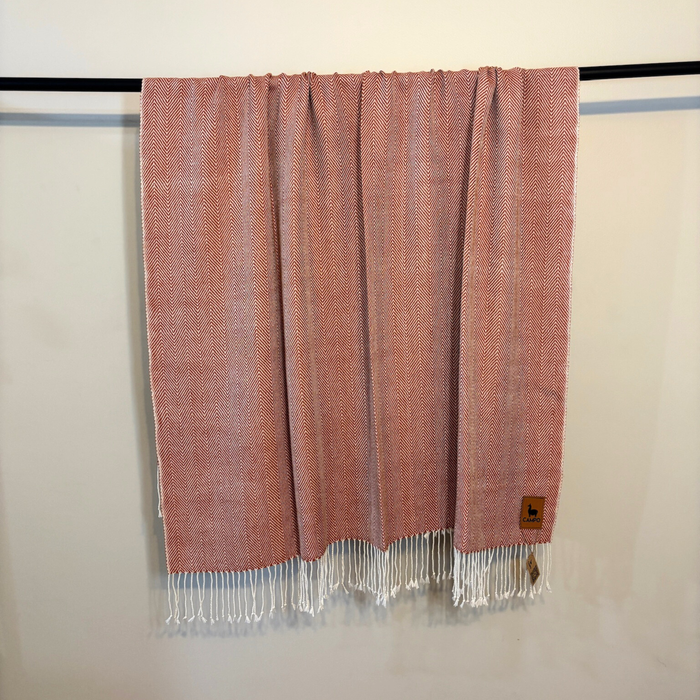 Red woven blanket with white fringe on a black rod against a beige wall.