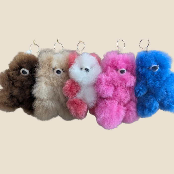 Five colorful fluffy keychains hanging on a beige background