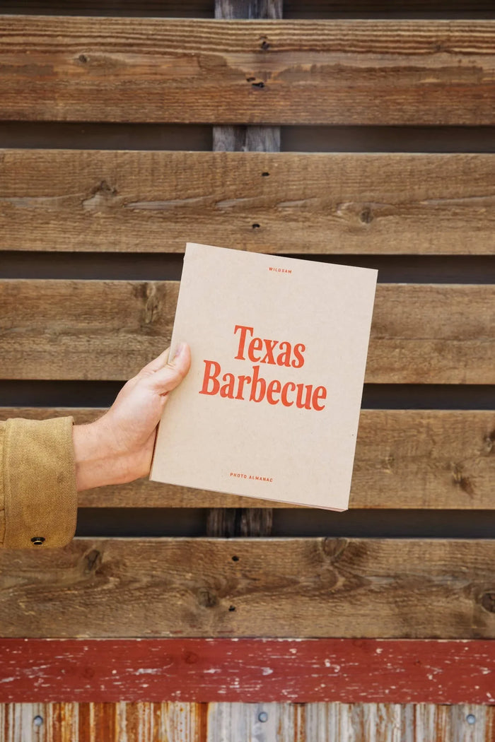 Front cover of Texas Barbecue photo almanac held in hand against wooden background