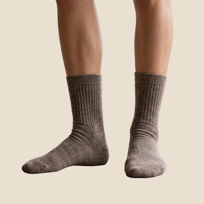 Person wearing brown socks standing on a light wooden floor.