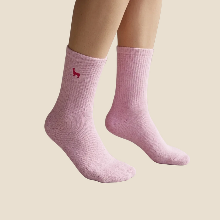 Pink socks with a small red logo worn indoors on a light wooden floor.