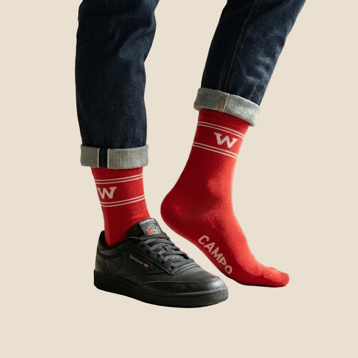 Red socks with a logo and text, worn with black sneakers on a beige background