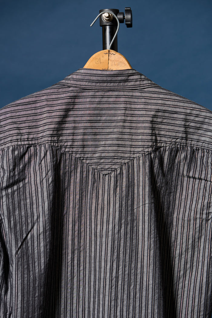 A gray and black vertically striped long-sleeve shirt shown from the back, hanging on a wooden hanger with a black studio stand against a dark blue background.
