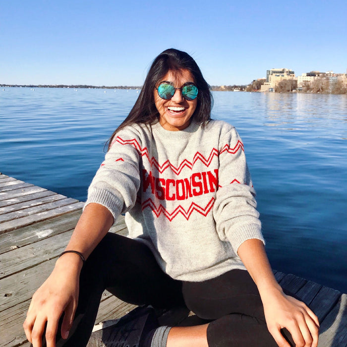 Person wearing a 'Wisconsin' sweater sitting on a dock by a lake.