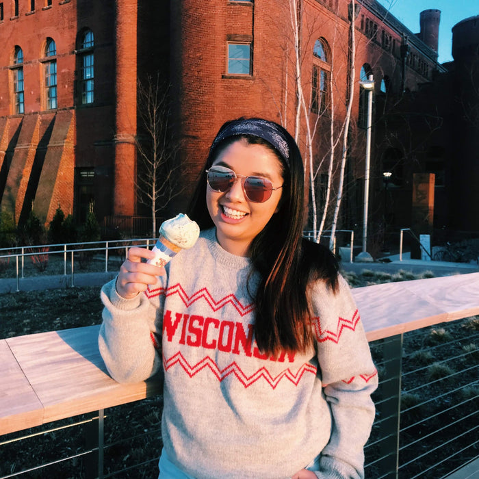 Person wearing a 'Wisconsin' sweater holding ice cream in front of a brick building.