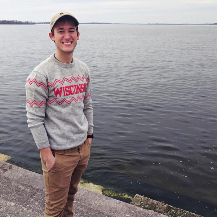Person wearing a gray 'Wisconsin' sweater by a body of water